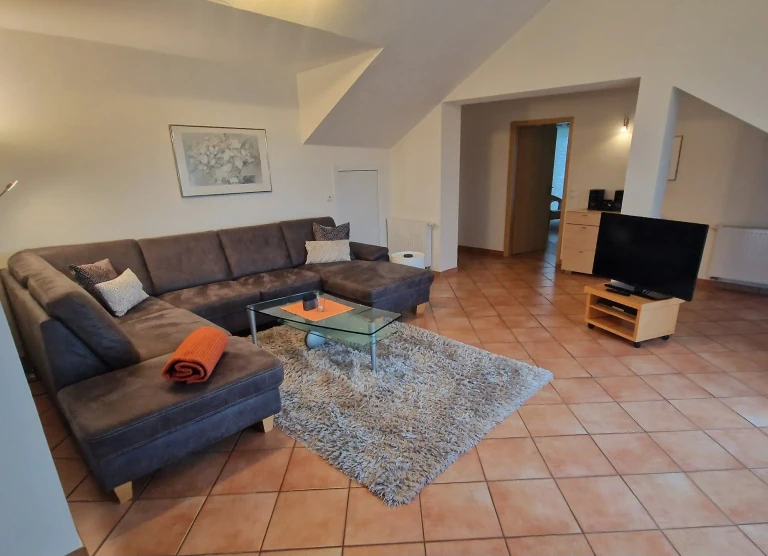 Großzügiges Wohnzimmer der Ferienwohnung Pfänder mit Ecksofa, TV-Bereich und heller Dachgeschossatmosphäre