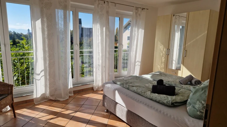 Sonniges Schlafzimmer der Ferienwohnung Säntis mit Doppelbett, großen Fenstern und Blick ins Grüne